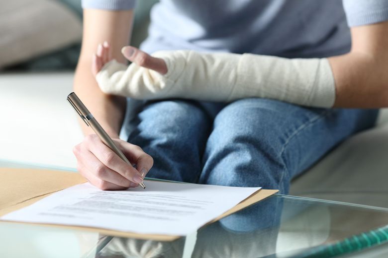 Person with a bandaged hand writing on a document at a glass table
