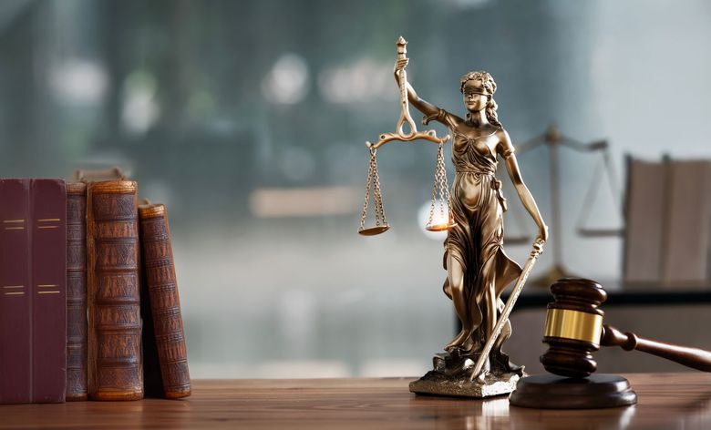 Law books, a Lady Justice statue, and a gavel on a wooden desk with a blurred background