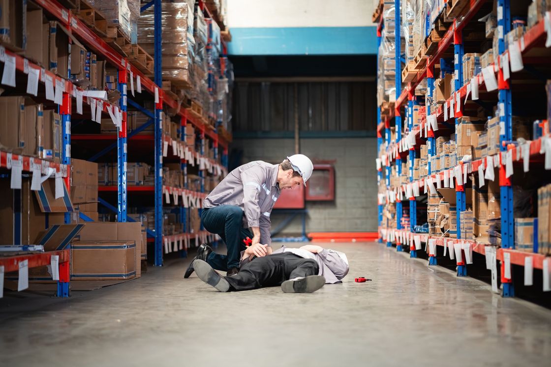 Worker seated on warehouse floor near boxes as a forklift approaches in the background