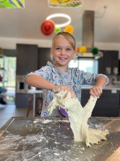 A little girl is playing with dough on a table.
