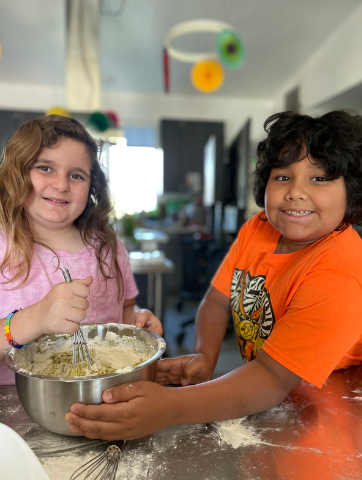 A boy and a girl are mixing ingredients in a bowl.