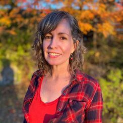 A woman in a red shirt and plaid shirt is smiling for the camera.