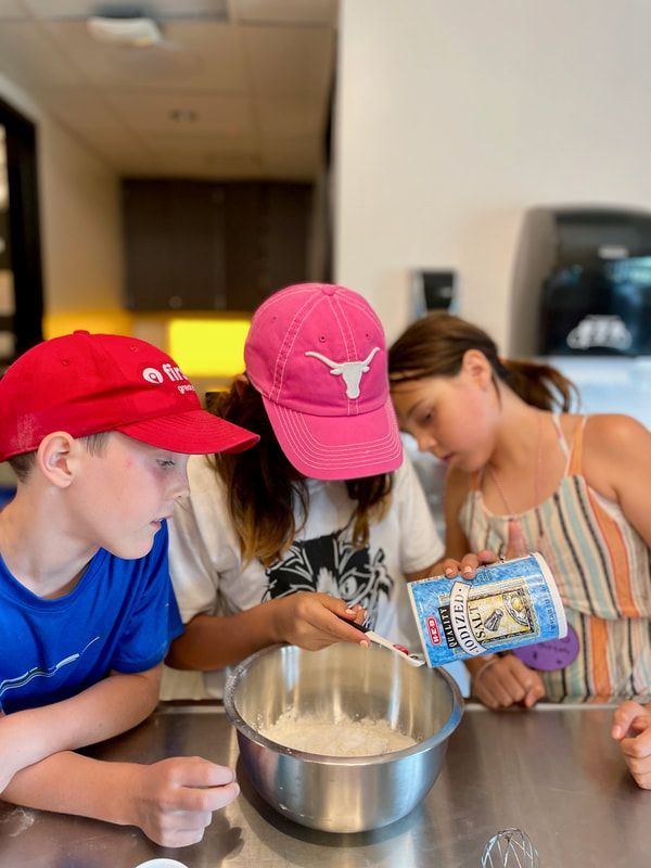 A group of children are sitting at a table preparing food.
