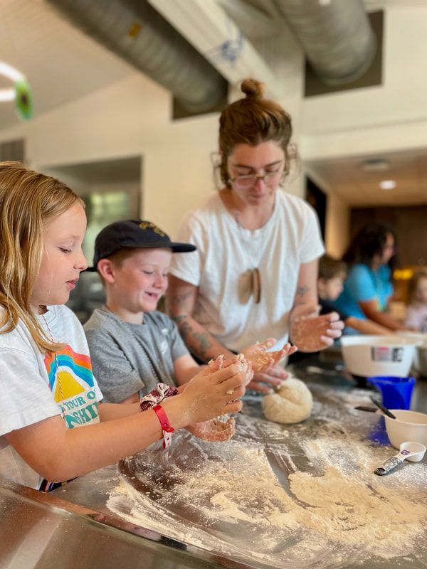 A woman and two children are kneading dough in a kitchen.