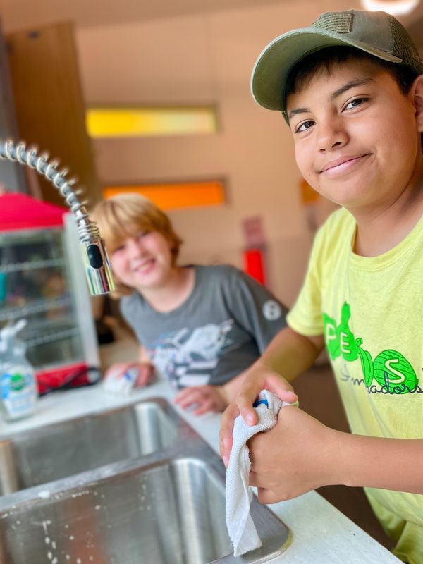 Two young boys are washing their hands in a kitchen sink.