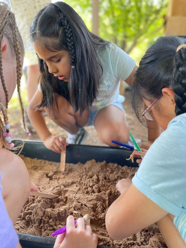 A group of young girls are playing in a sandbox.