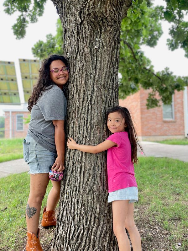 A woman and a little girl are hugging a tree.