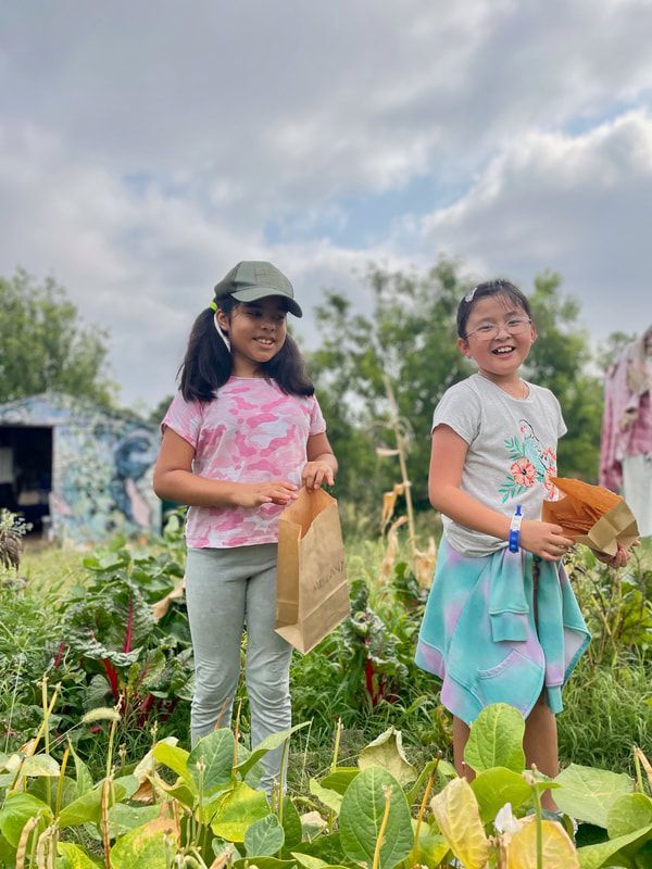 Two young girls are standing in a field holding bags of vegetables.