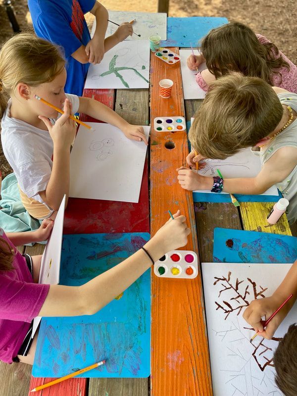 A group of children are sitting at a table painting with watercolors.