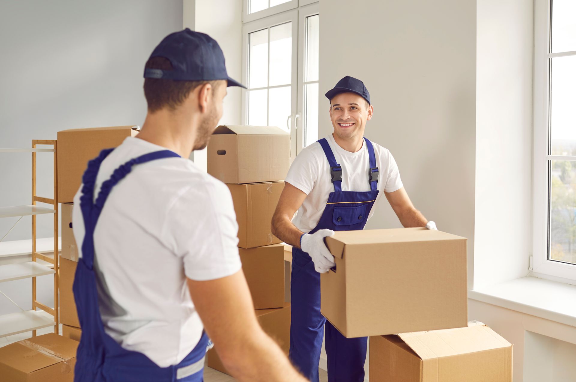 Cheerful full-service movers are carrying cardboard boxes together.