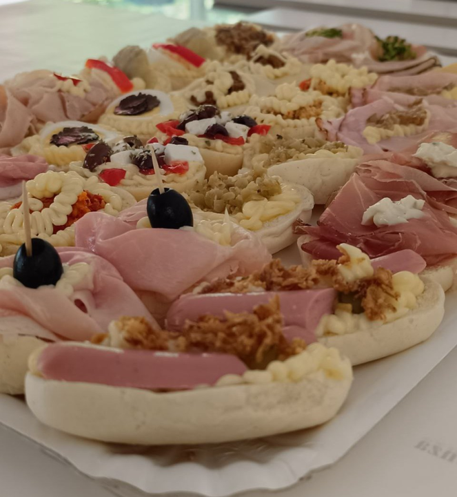 Vassoio di piccoli panini con vari condimenti: prosciutto, formaggio, olive e verdure.