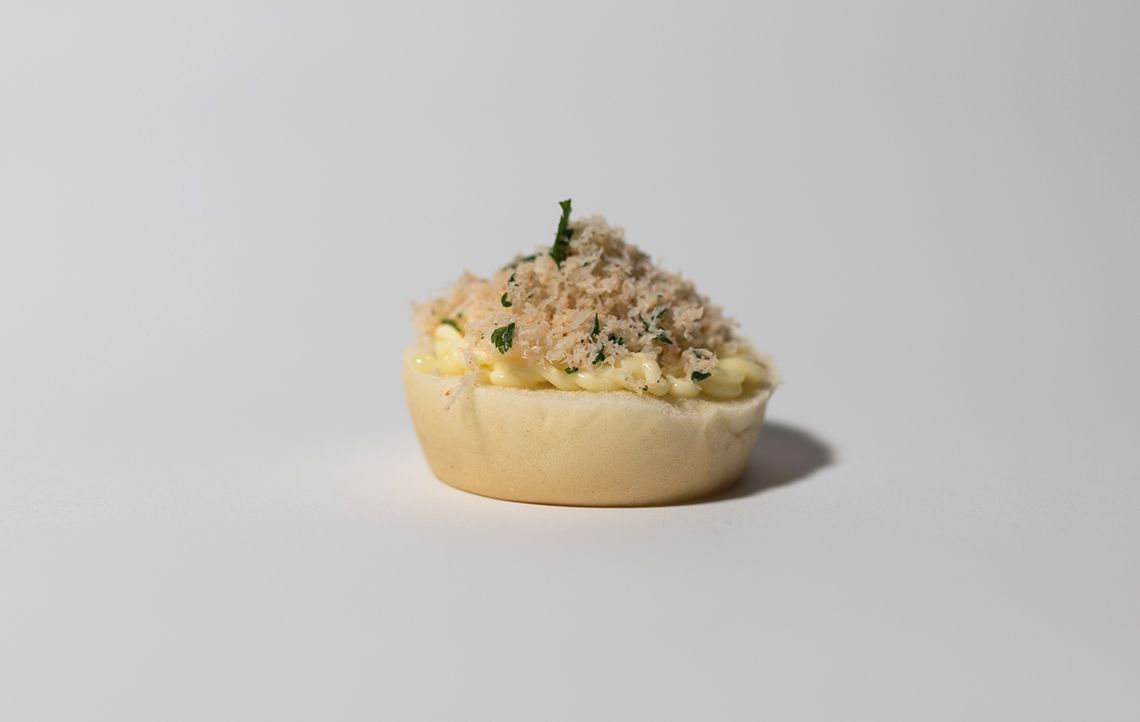 Piccola tazzina di pane ripiena di insalata di uova, guarnita con carne di maiale sfilacciata e un rametto di prezzemolo.