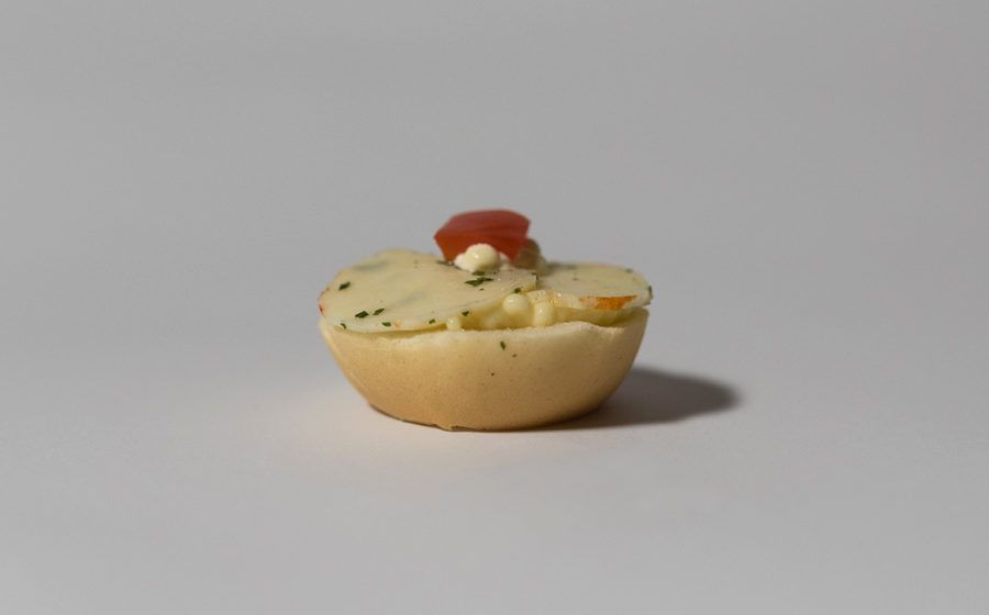 Piccolo antipasto in una tazza di pane cotto al forno, guarnito con ripieno bianco, erbe aromatiche e una guarnizione rossa.