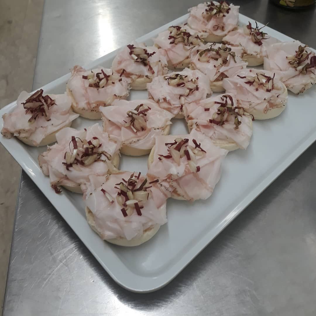 Antipasti su un piatto bianco: piccole fette di pane ricoperte di salumi e guarnizioni.