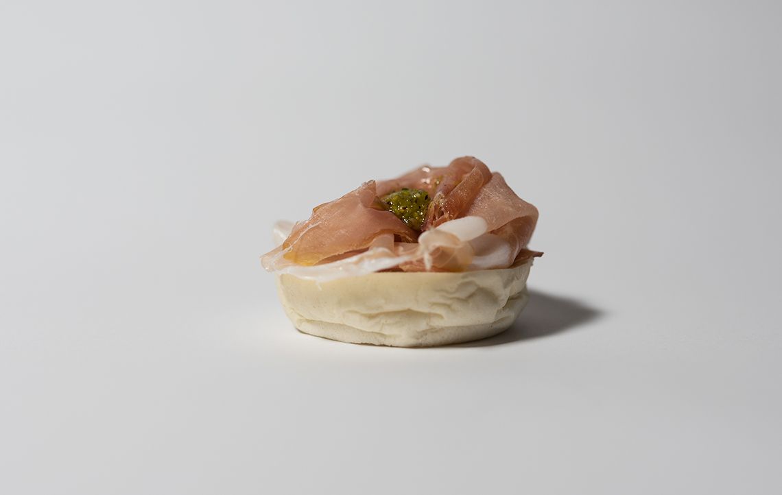 Antipasto su sfondo bianco, pane rotondo con carne e guarnizione verde sopra.