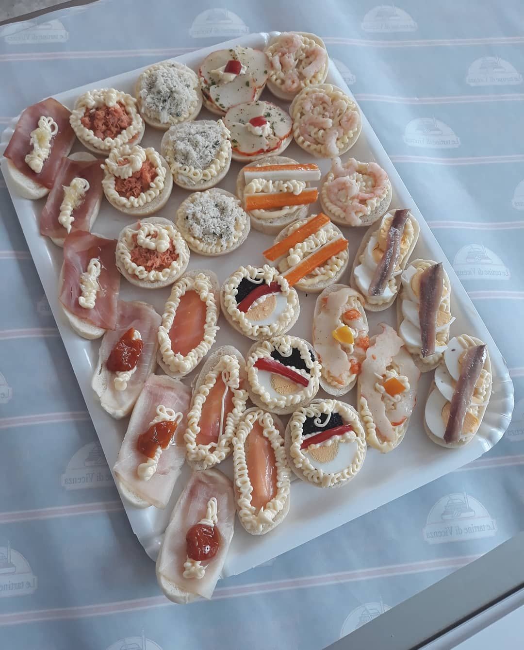 Vassoio di vari antipasti, tra cui prosciutto, gamberi e acciughe, su una superficie decorata.