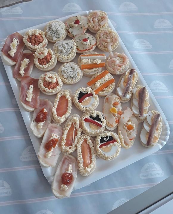 Vassoio di vari antipasti, tra cui prosciutto, gamberi e acciughe, su una superficie decorata.