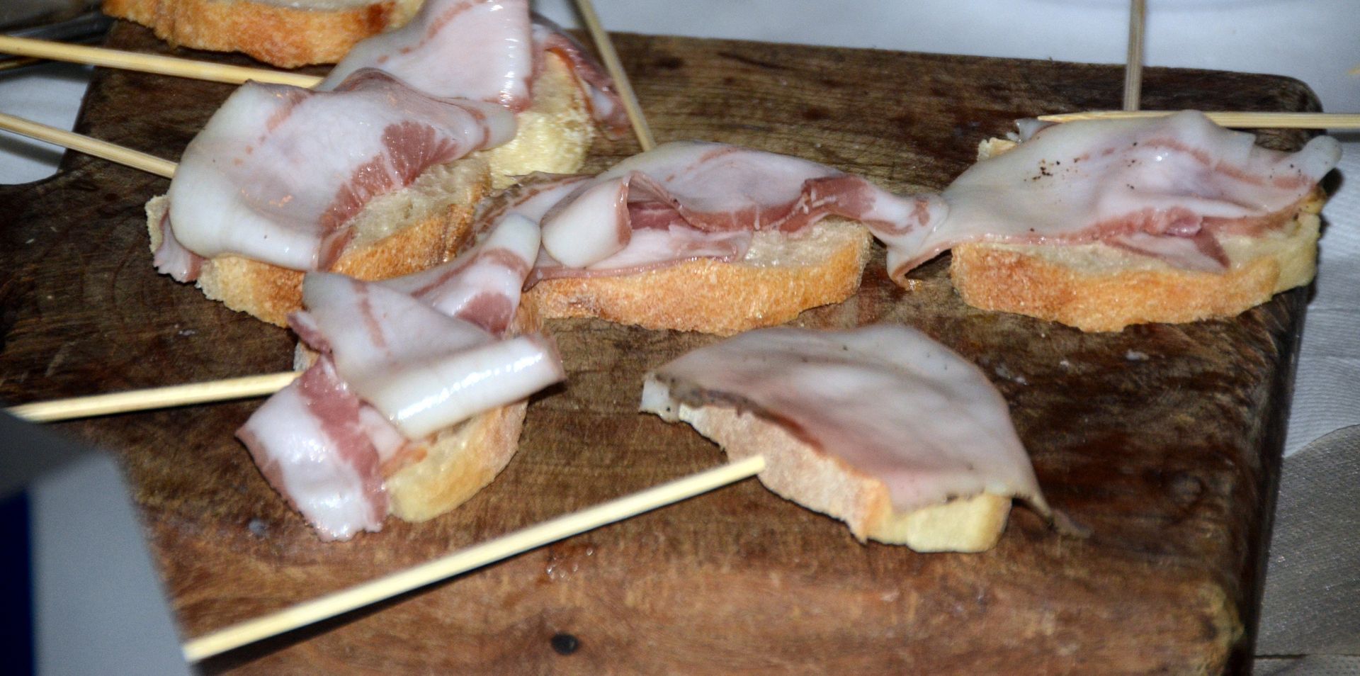 Antipasti di pancetta e pane su un tagliere di legno, tenuti insieme con stuzzicadenti.