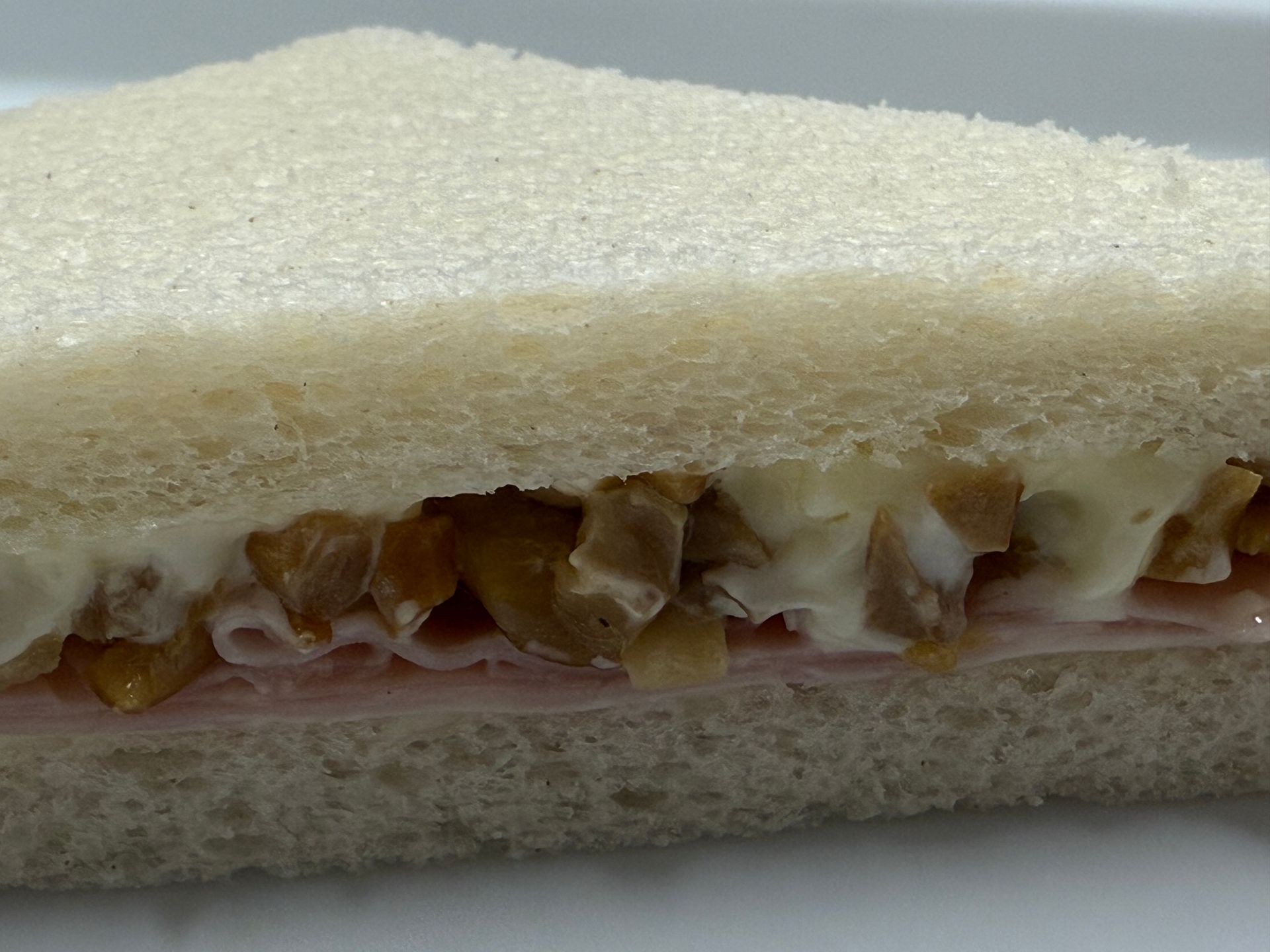 Panino triangolare con prosciutto, salsa cremosa e ingredienti tritati, racchiuso tra pane bianco.