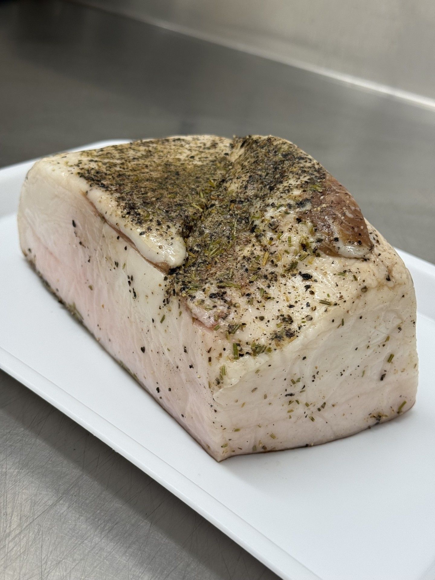 Blocco di pancetta di maiale condita su un vassoio bianco, pronto per la cottura.