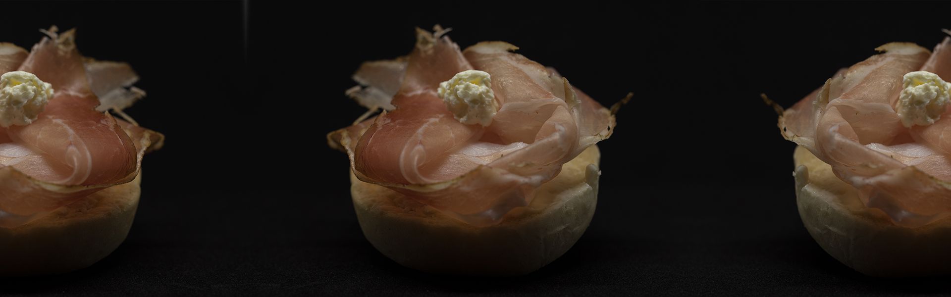 Tre piccoli antipasti conditi con salumi e un cucchiaio di besciamella. Sfondo scuro.