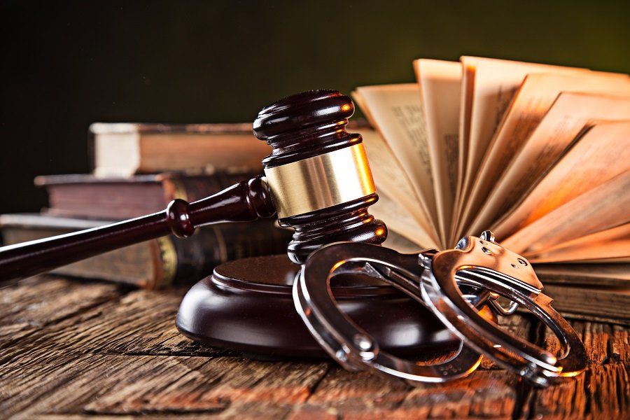 a gavel resting against a pair of handcuffs and a legal book on a desk