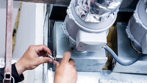 A person is fixing a ventilation system with a wrench.