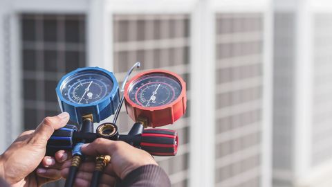 A person is holding a pressure gauge in front of a building.