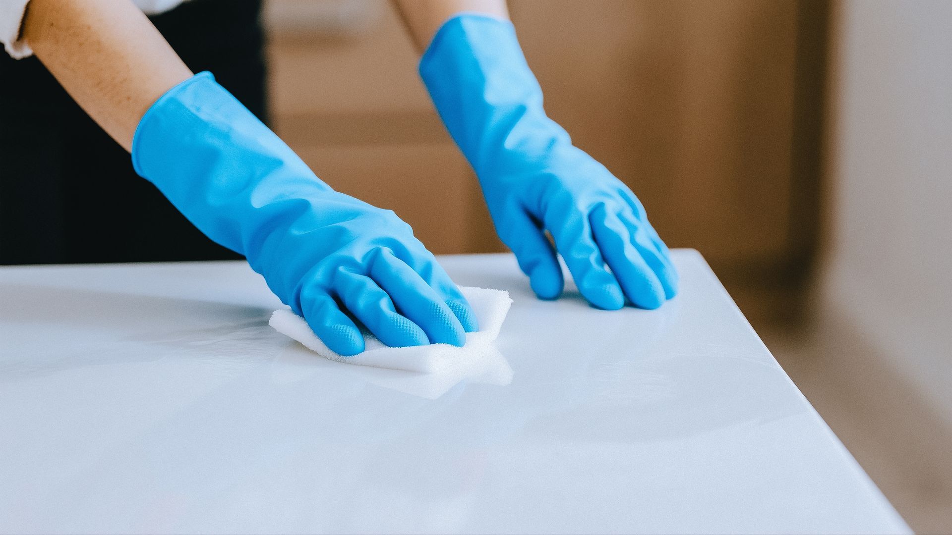 Blue-gloved hands wiping a white surface with a cloth