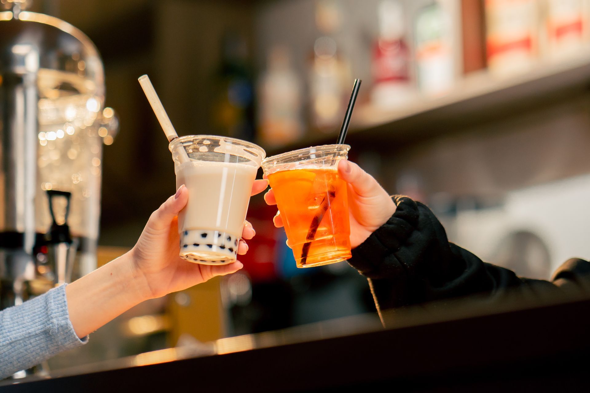 Close up of a cup of orange drinks and a cup of boba milk tea holding by 2 people's hands