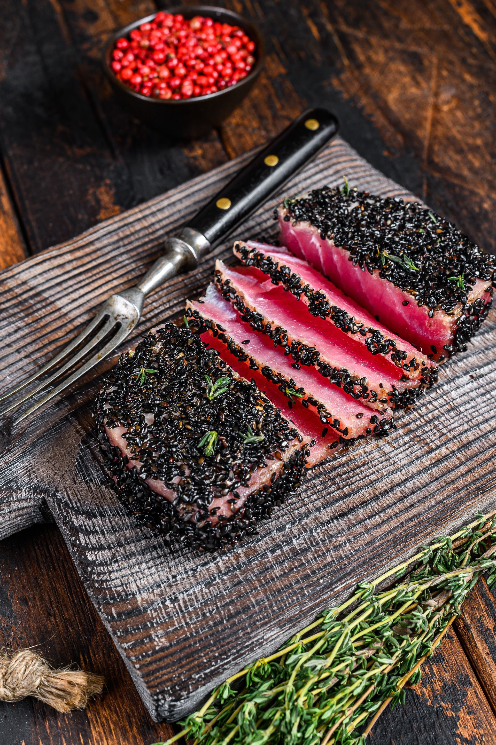 Home-made cut grilled sesame tuna steak on a cutting board, with a folk on the side