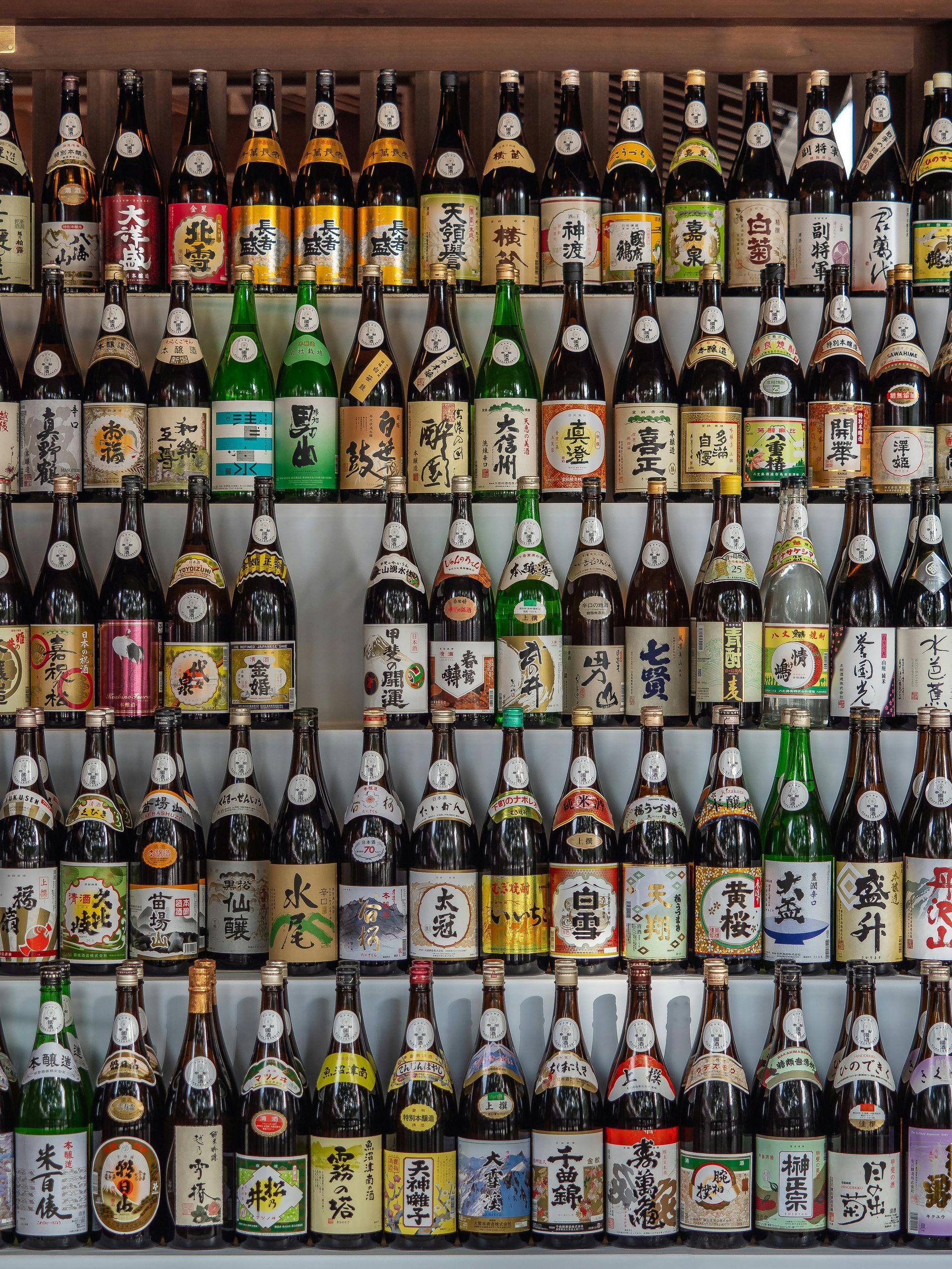 A wall of Japanese sake bottles on shelves, showcasing various labels and designs