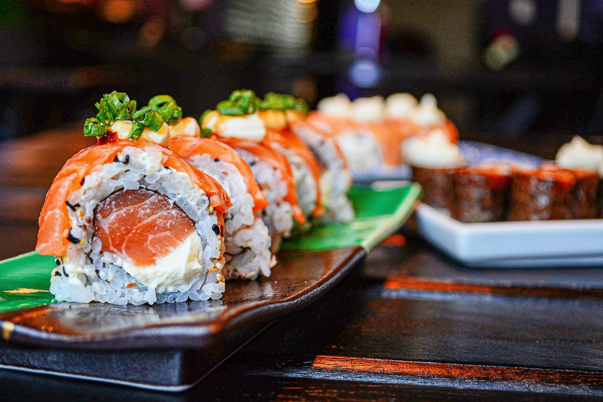 Close up of a salmon sushi roll and a plate of sushi roll on background.