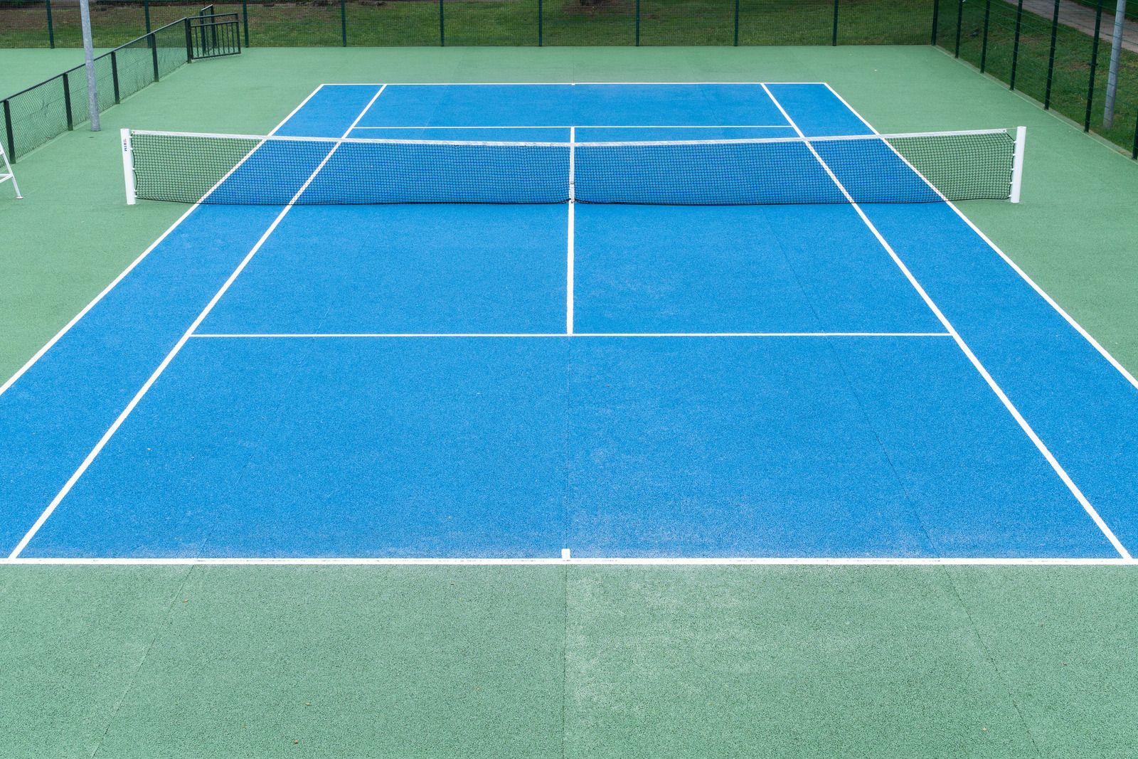 Blue tennis court with white lines and net, green surrounding area.
