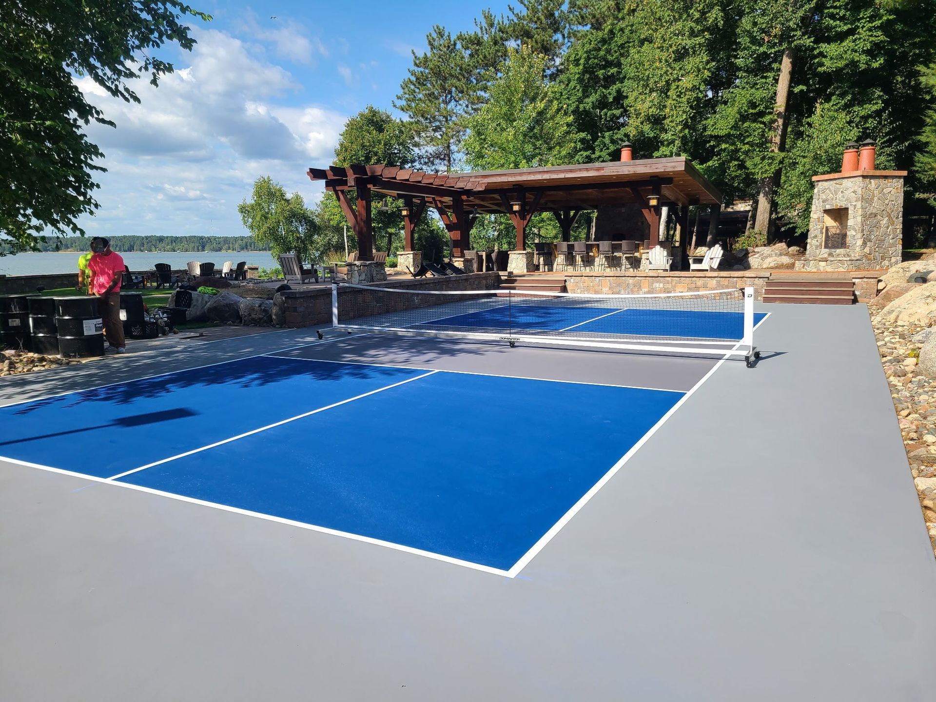 Blue and gray pickleball court with net, pergola, and view of water.