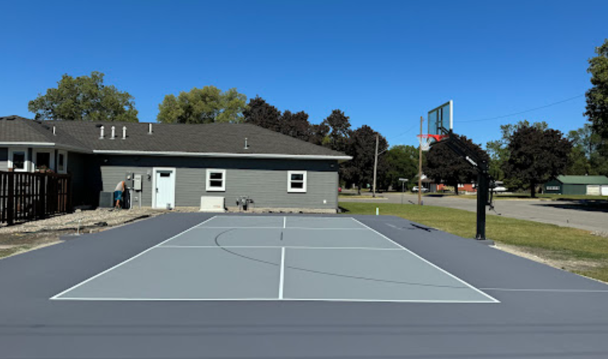 A basketball court in front of a house on a sunny day