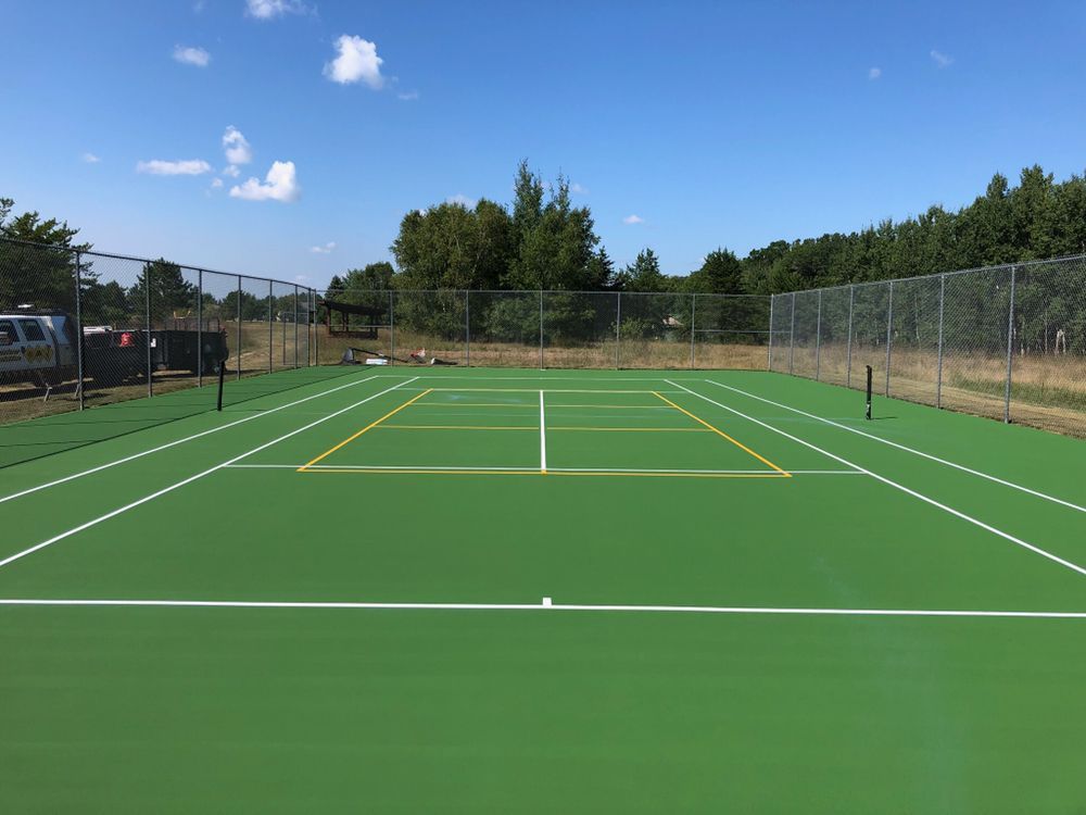 A green tennis court with white lines and a fence in the background.