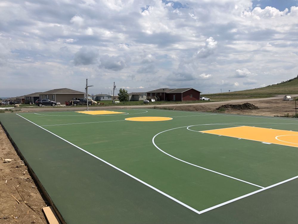 A green and yellow basketball court with houses in the background.