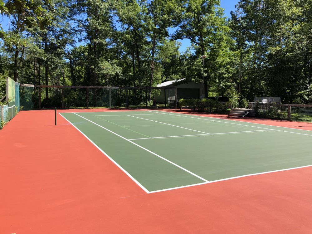 A tennis court is surrounded by trees on a sunny day.