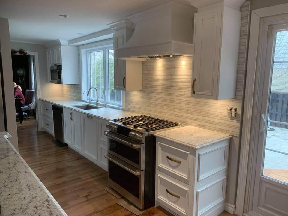 Cuisine blanche avec appareils électroménagers en acier inoxydable, parquet en bois clair et fenêtre avec vue.