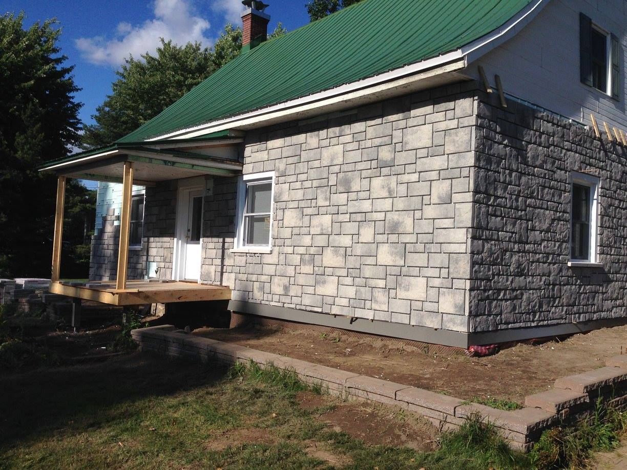 Une maison en pierre avec un toit vert et un porche.