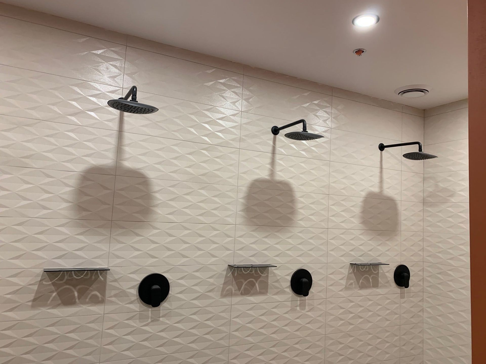 Une salle de bain avec trois pommeaux de douche au mur.