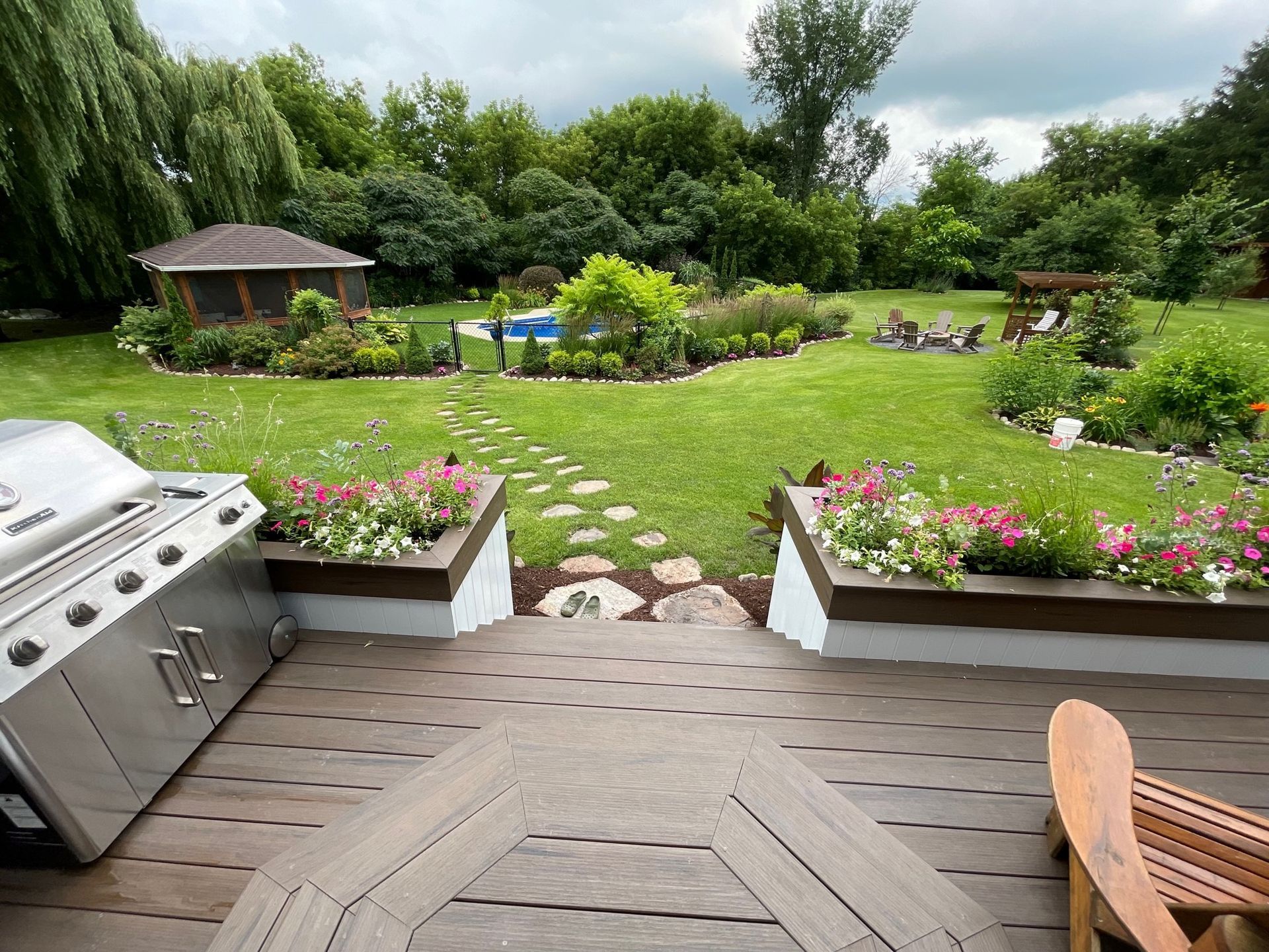 Une terrasse en bois avec un grill et des chaises devant une cour verdoyante.