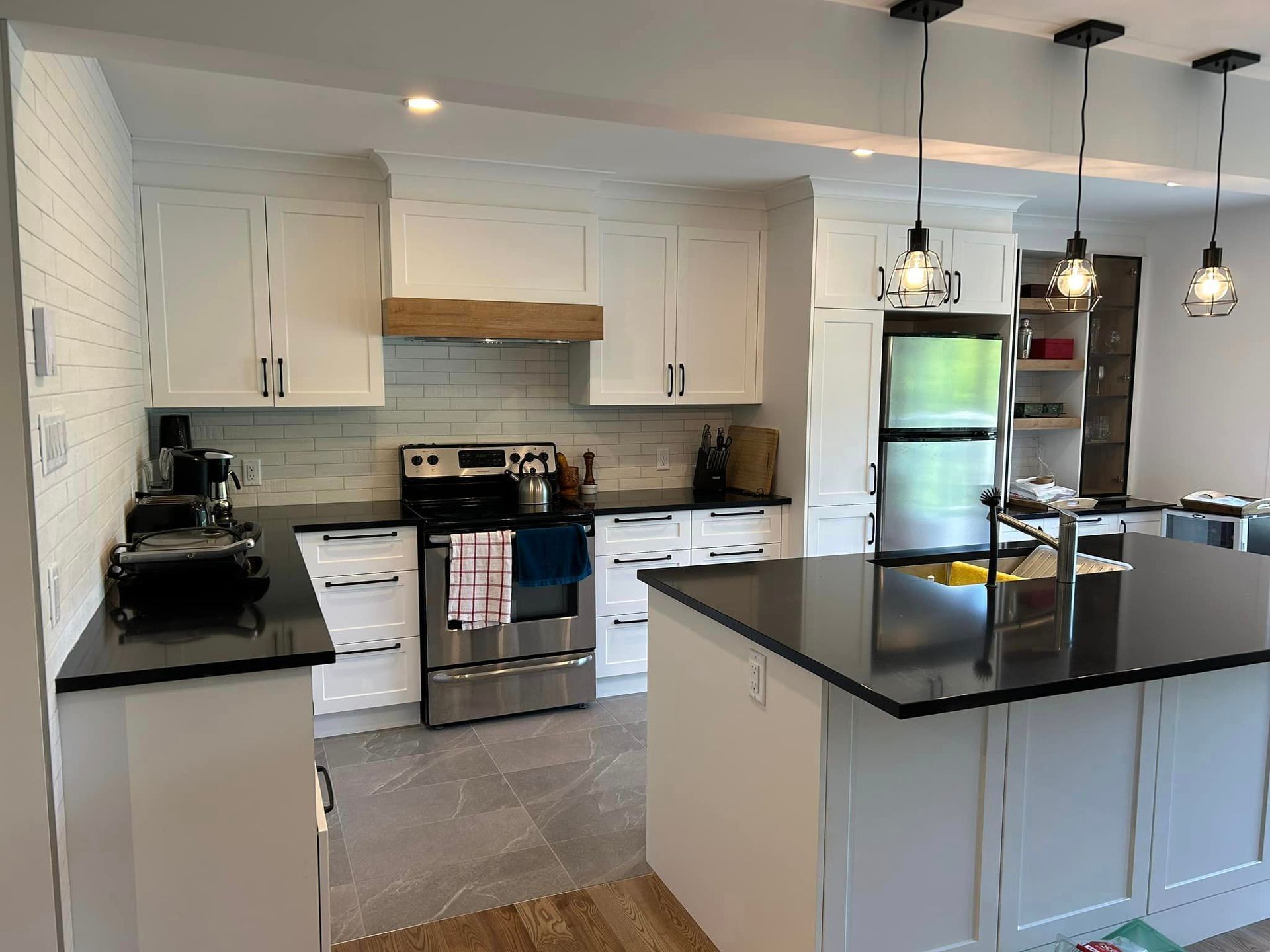 Une cuisine avec armoires blanches, comptoirs noirs, électroménagers en acier inoxydable et un grand îlot.