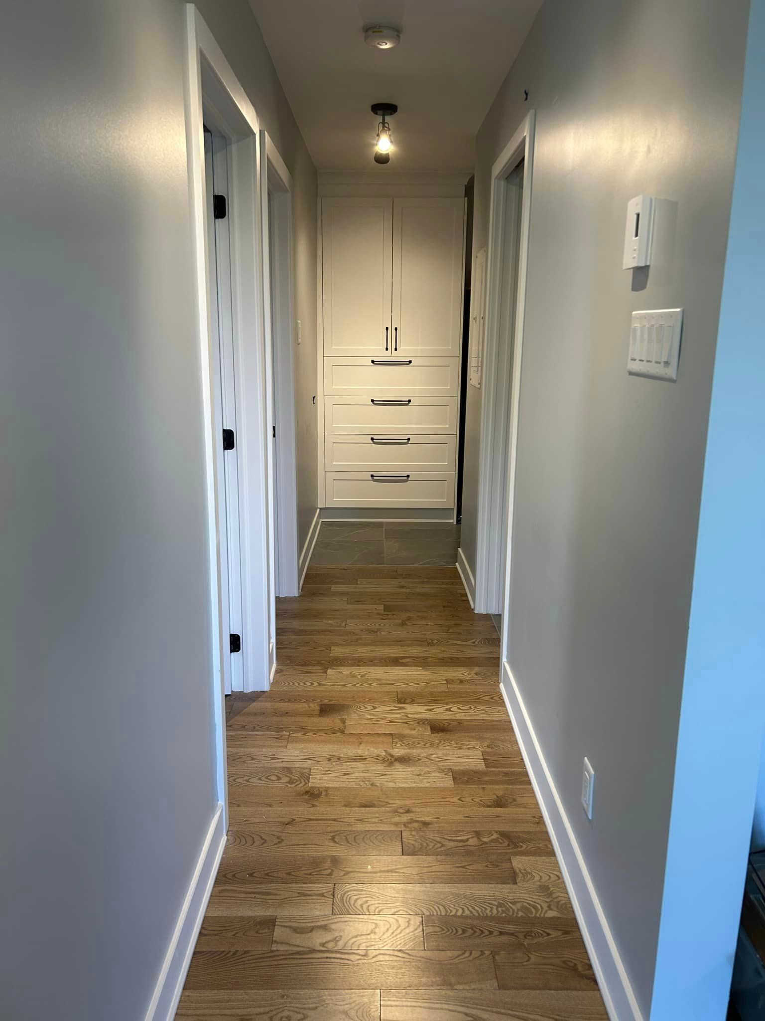 Un long couloir avec parquet et murs blancs dans une maison.