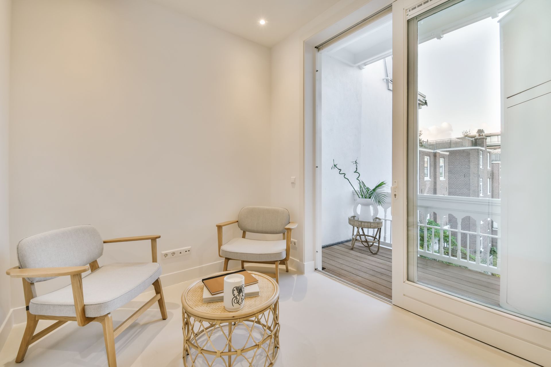 Deux chaises et une petite table dans une pièce lumineuse, avec un balcon visible à travers une porte coulissante en verre.