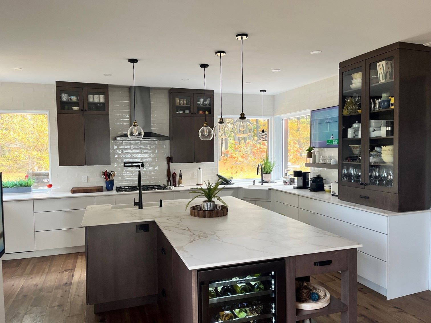Cuisine moderne avec armoires brun foncé, comptoirs blancs et un grand îlot avec un refroidisseur à vin.