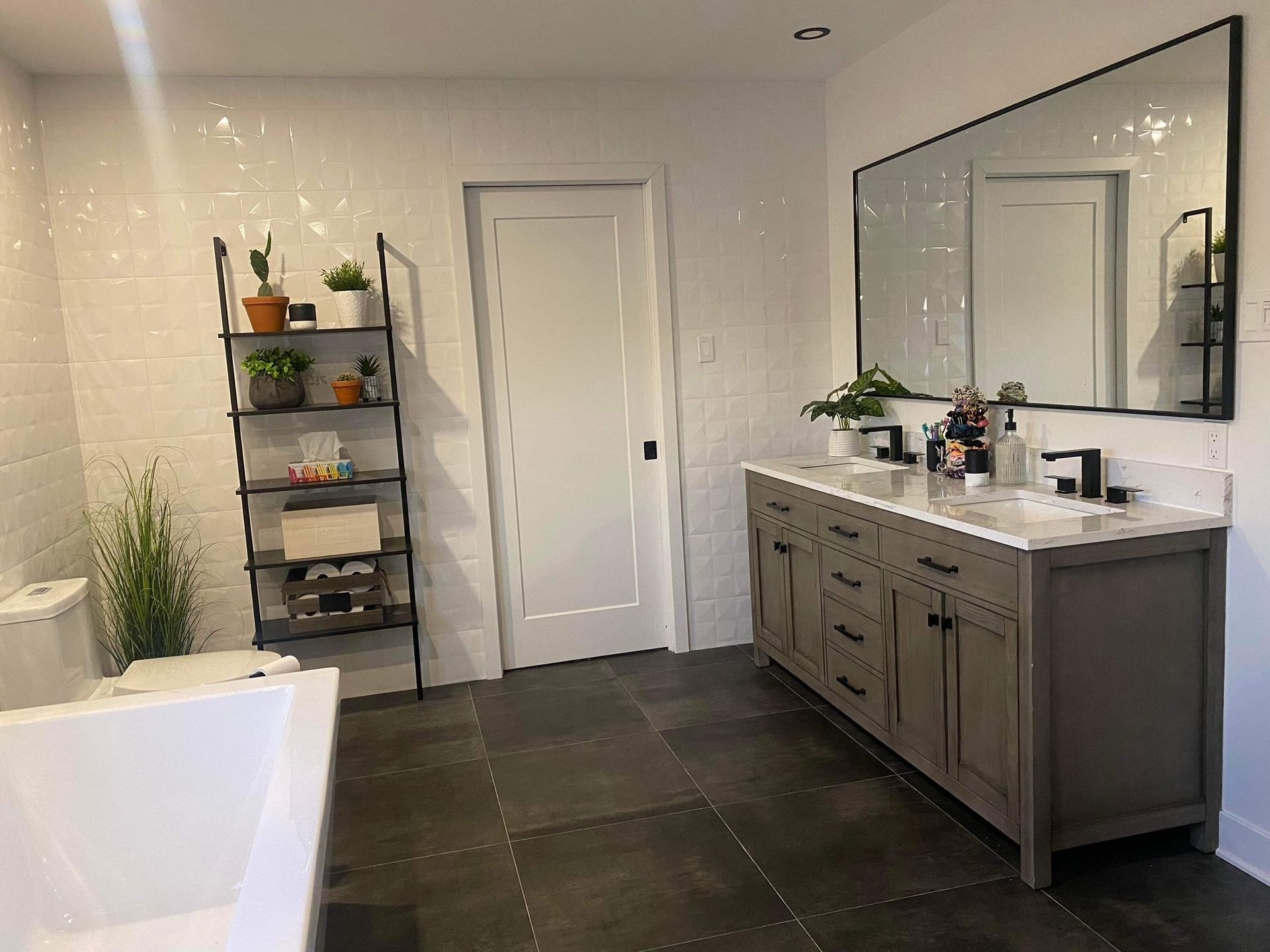 Une salle de bain moderne avec une baignoire blanche, une vanité grise et une étagère en métal noir.