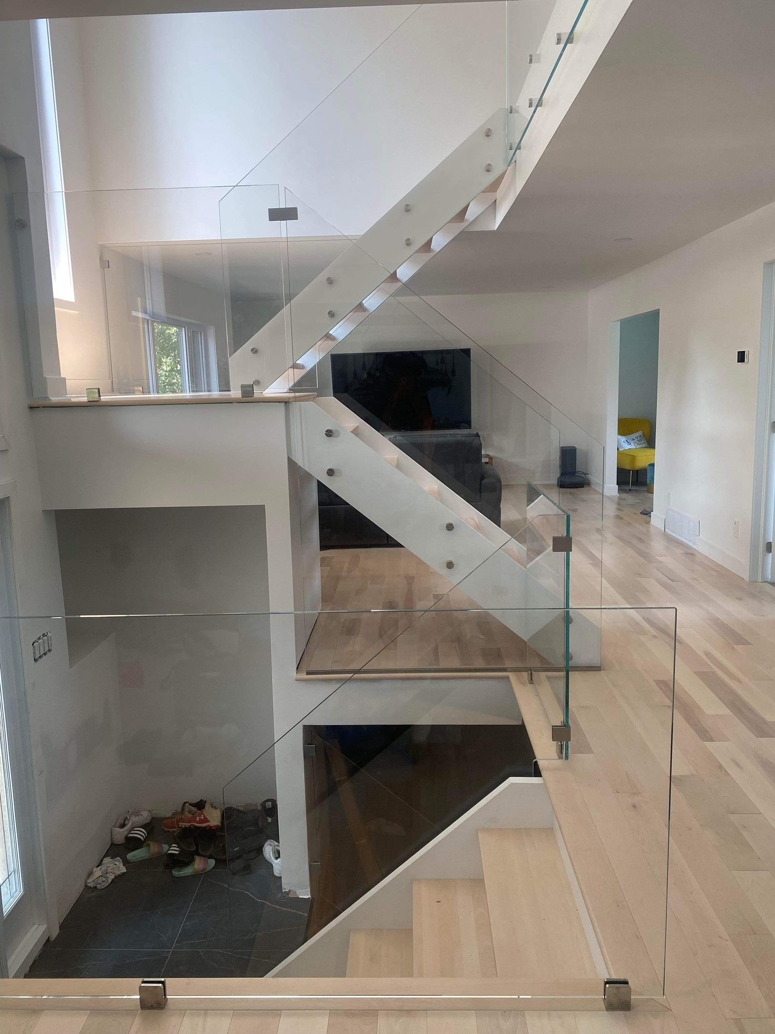 Intérieur de maison moderne avec un escalier à rampe en verre dans un espace lumineux avec parquet.