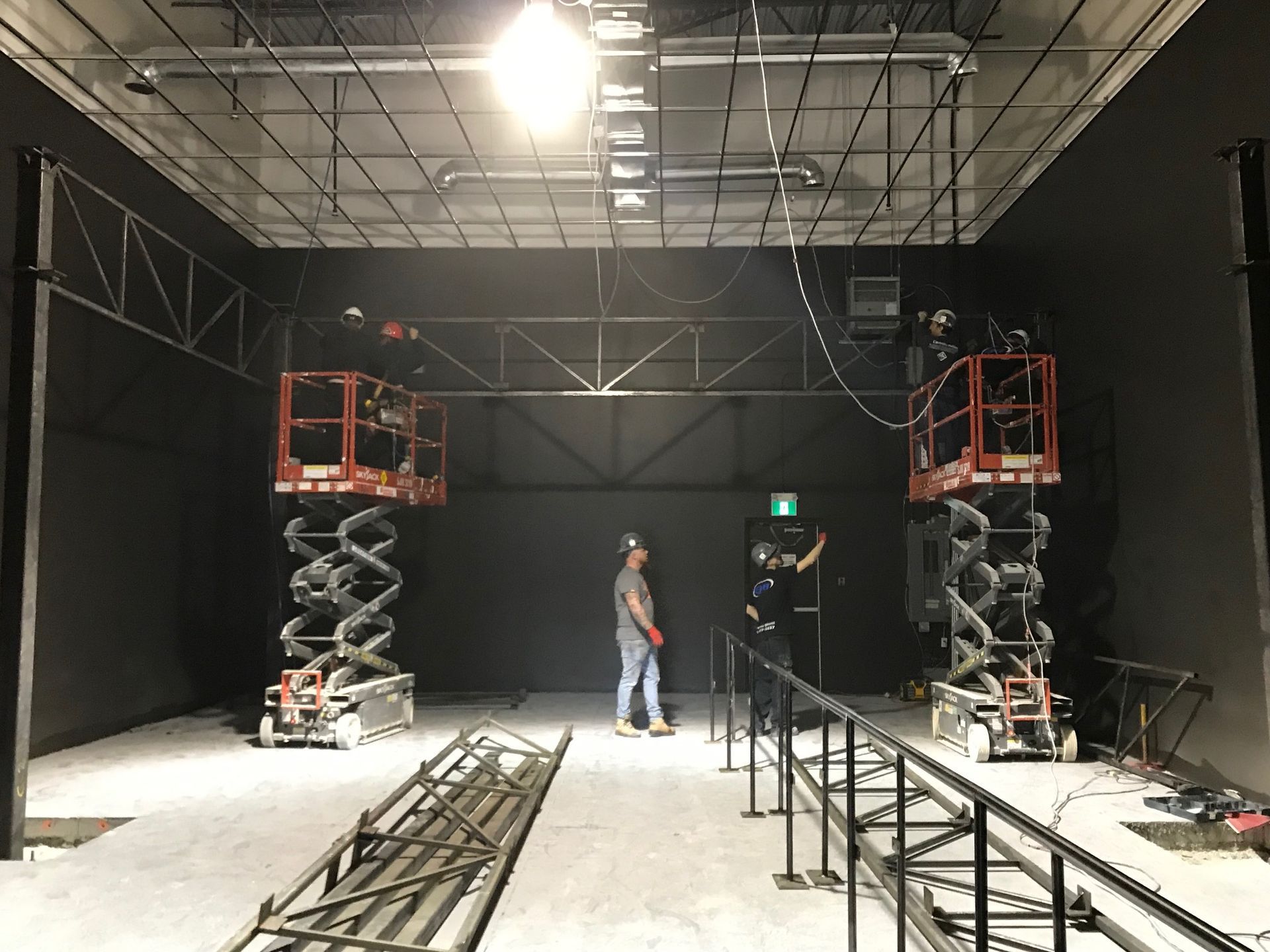 Deux élévateurs à ciseaux avec des ouvriers dans un théâtre sombre, équipement de gréement visible.